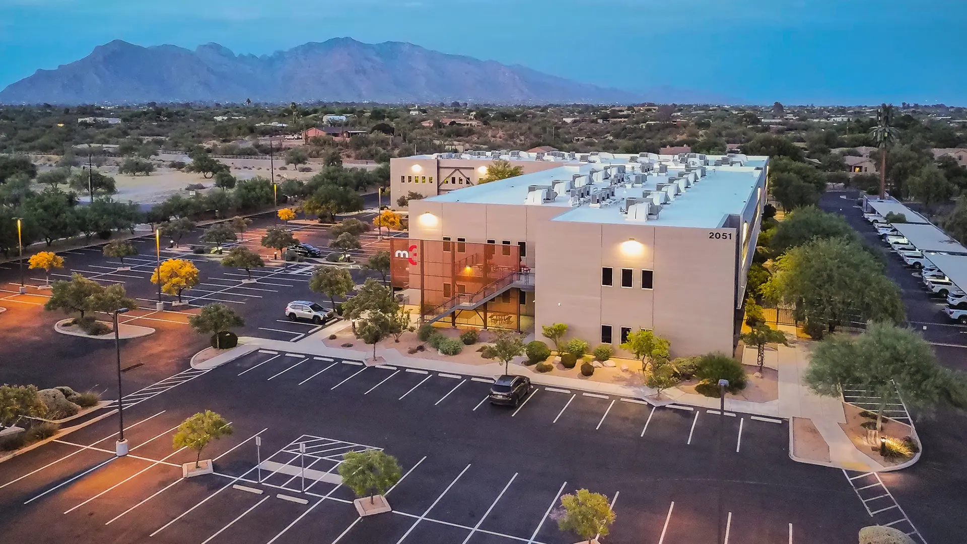 Commercial Real Estate and Property Management of the M3 building that is sat within a sprawling car park set against the mountains in Tucson at dusk.